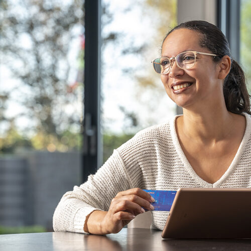 Vrouw aan tafel met betaalpas achter laptop - Internetbankieren